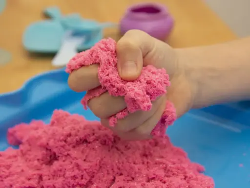 Kind hält pinken kinetischen Sand, der sich leicht formen lässt. Perfekt zum **kinetic sand selber machen** und Spielen.