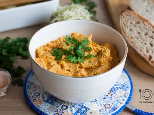 Pyszna pasta z kurczaka w miseczce, udekorowana natką pietruszki, obok czosnek i kromki chleba.
