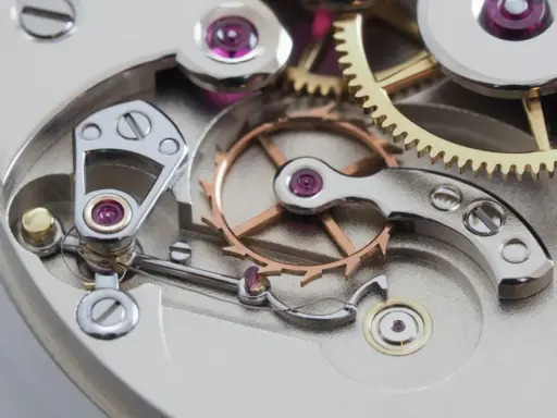 Meccanismo di orologio con ingranaggi dorati e ruota bilanciere, parte di uno scappamento coassiale.
