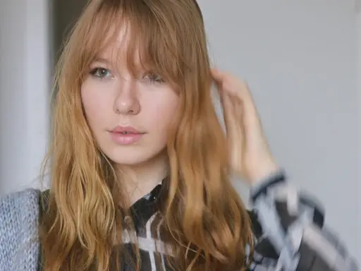 Ein junges Mädchen mit langen, welligen Haaren und Pony, das sich die Haare stylt.