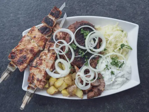 Ein Teller mit gegrilltem Fleisch, Kartoffeln und Krautsalat, garniert mit Zwiebelringen. Ein authentisches Souvlaki Rezept original.