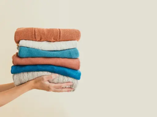 Hände halten einen Stapel bunter Pullover. Eine gute Idee für waschmittel ersatz, wenn man die Kleidung schonend behandeln möchte.