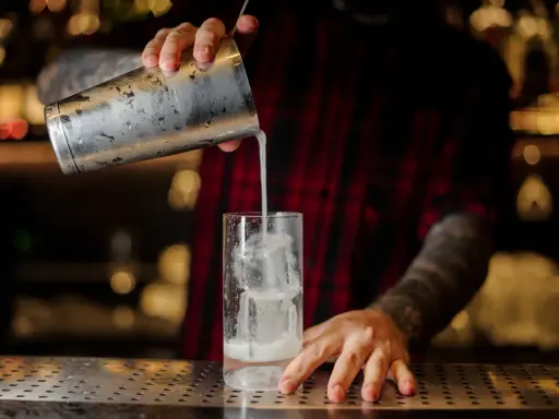 Barkeeper gießt einen erfrischenden Gin Fizz mit Eis in ein Glas.