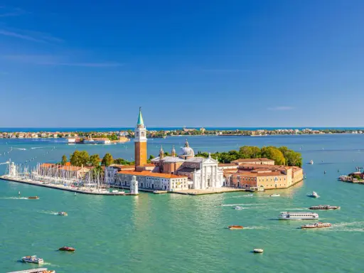 Vue aérienne de Venise, le campanile San Giorgio Maggiore se dresse fièrement sur son île, entouré d'eaux turquoise et de voiliers.