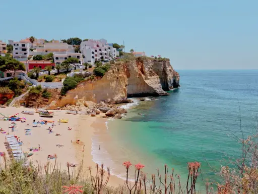 Sonnige Küste Portugals mit weißem Strand, türkisfarbenem Meer und Häusern auf den Klippen. Perfekt für eine Portugal Wetter Jahresübersicht.