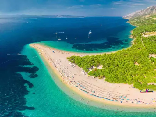 Plaża w kształcie języka, otoczona turkusową wodą i zielonym lasem, z widokiem na góry.