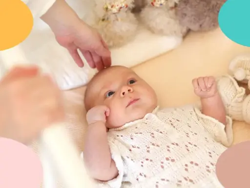 Un bebé despierto en su cuna, con una mano acariciándole la cabeza. Parece que mi bebe tarda mucho en dormirse.