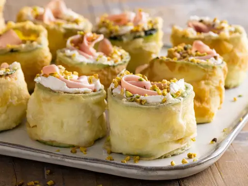 Rotolini di zucchine impanate e fritte, farciti con crema, prosciutto e pistacchi. Stuzzichini veloci ed economici perfetti per un aperitivo sfizioso.