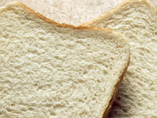 Zwei Scheiben Weißbrot liegen auf einem Holzbrett. Die Frage "wie viel Kalorien hat eine Scheibe Toast?" beschäftigt viele.