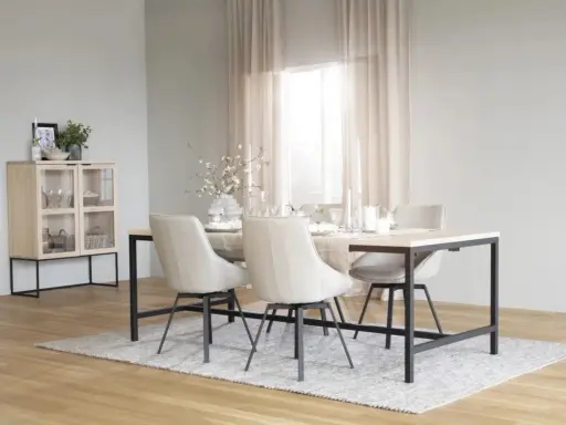 Ett ljust och luftigt rum med matbord och stolar i nordisk design. Ett vitrinskåp i trä och metall står till vänster.