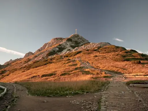 Szlak na Giewont z dzieckiem. Kamienna ścieżka wije się po zboczu oświetlonym słońcem, prowadząc ku szczytowi z krzyżem.