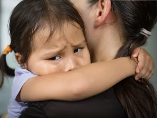 Ein Kind weint im Kindergarten und klammert sich an seine Mutter. Die Kleine hat Tränen in den Augen und sucht Trost.