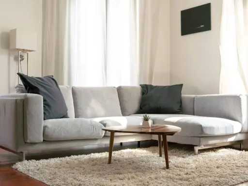 Un cómodo cheslón gris con cojines oscuros, alfombra mullida y mesa de centro de madera.