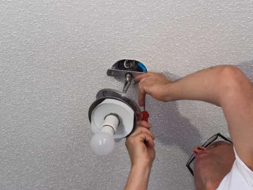 Un homme installe un luminaire au plafond avec un tournevis.
