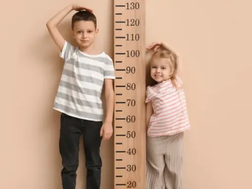 Chłopiec i dziewczynka mierzą wzrost przy drewnianej miarce. Chłopiec ma ok. 115 cm, dziewczynka ok. 85 cm. Rozmiar 68 jaki wiek?