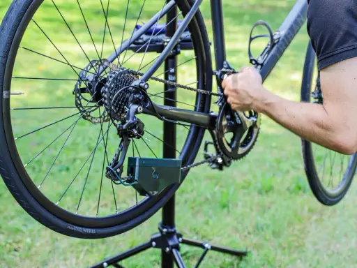 Rowerzysta zakłada łańcuch w rowerze z przerzutkami. Pokazano tylną przerzutkę, kasetę i korbę.