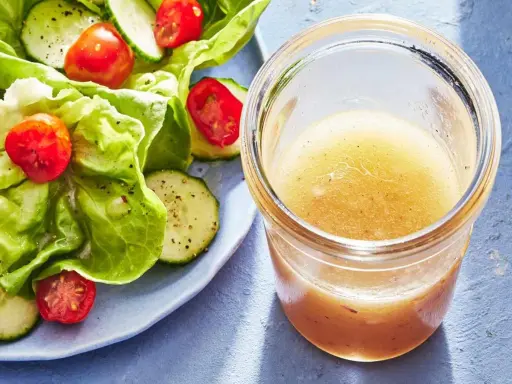 En burk med hemlagad salladsdressing bredvid en fräsch sallad med gurka och tomater. Ett perfekt salladsdressing recept för en lätt lunch.