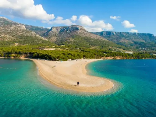 Spiaggia a forma di lingua di sabbia dorata, bagnata da acque cristalline, con montagne verdi sullo sfondo. Un angolo di paradiso in **Croazia mare**.