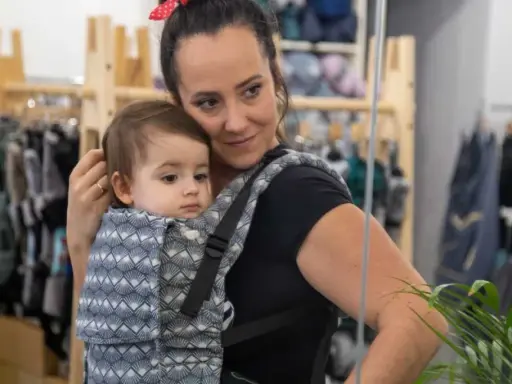 Mama wybiera jakie nosidełko dla 5 miesięcznego niemowlaka. Dziecko w nosidle z wzorem.
