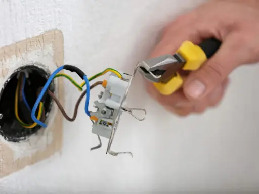 Mainteneur ajustant un fil bleu et marron dans une prise électrique.