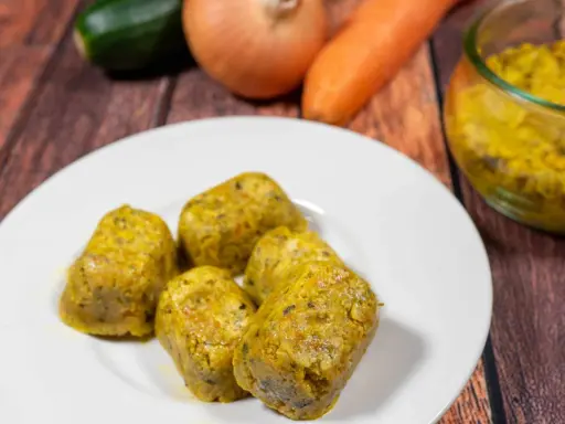 Cinque cubetti dorati di dado vegetale fatto in casa, preparati con carote, zucchine e cipolle, su un piatto bianco.