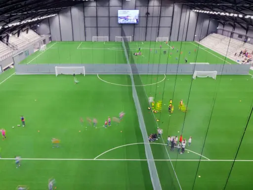 Barn tränar fotboll på en grön konstgräsplan i Prioritet Serneke Arena. Publik sitter på läktaren.