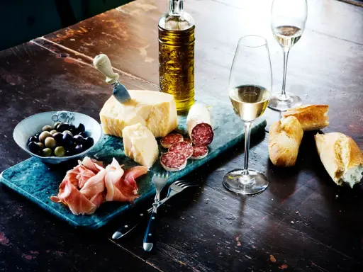 En härlig italiensk buffé med ost, salami, prosciutto, oliver, bröd och ett glas vitt vin, kanske en riesling druva.
