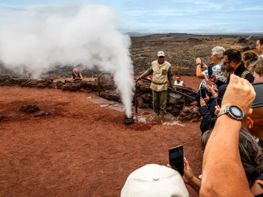 Touristen bestaunen im Nationalpark Timanfaya eine Dampf-Demonstration. Ein Führer gießt Wasser in ein Loch, das sofort zu Dampf wird.