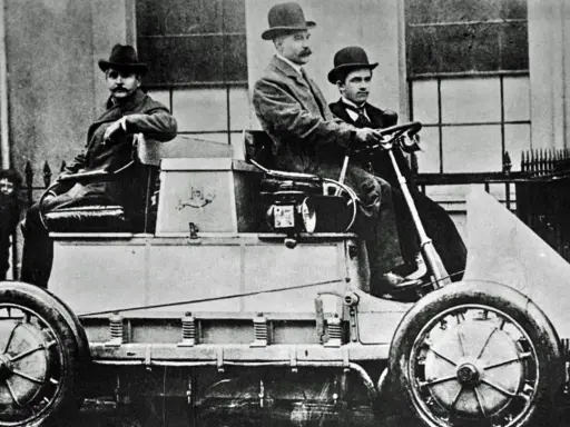 Hombres con sombreros posan en el primer coche eléctrico de la historia, un vehículo pionero de finales del siglo XIX.