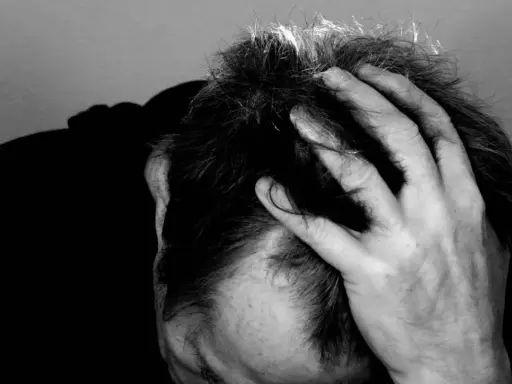 Uomo con mano tra i capelli, ombra scura sul volto. Potrebbe rappresentare il peso di una diagnosi di linfoma cutaneo.