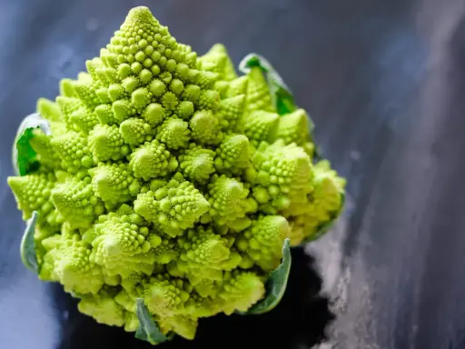Un chou romanesco d'un vert éclatant, aux spirales parfaites, se dresse sur un fond sombre et texturé.