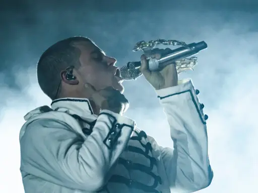 Artysta w białej kurtce z czarnymi zdobieniami śpiewa do mikrofonu. Te rap wspomnienia na zawsze w sercu.