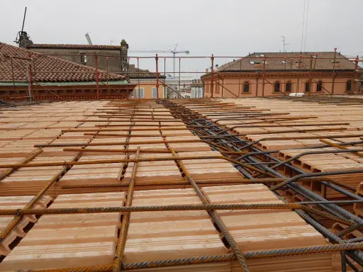 Posa di armature su tavelloni in laterizio, con sullo sfondo facciate in pietra e mattoni di edifici storici.
