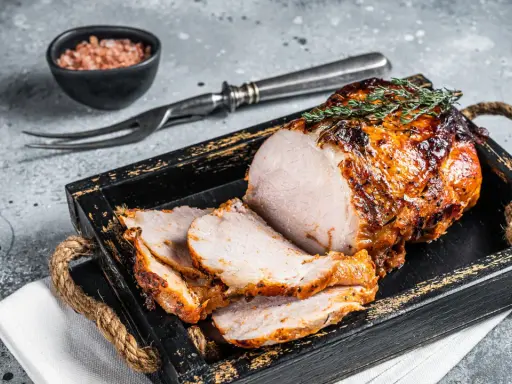 A sliced, roasted pork loin with a golden-brown crust, garnished with thyme, on a rustic wooden tray.