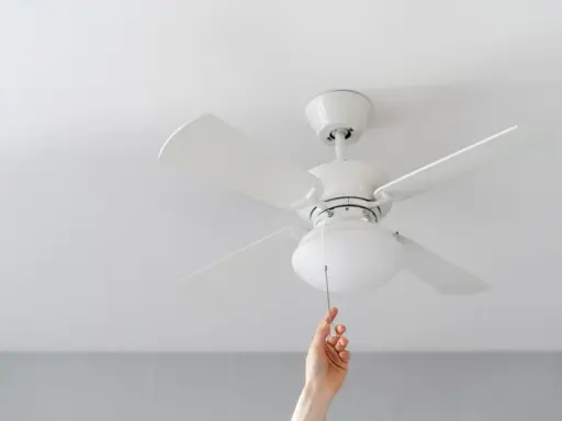 Mano tira de la cadena de un ventilador de techo pladur blanco, iluminando la habitación.