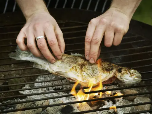 Hände legen einen Fisch auf den Grill. Mit etwas Übung gelingt das Fisch grillen ohne kleben.