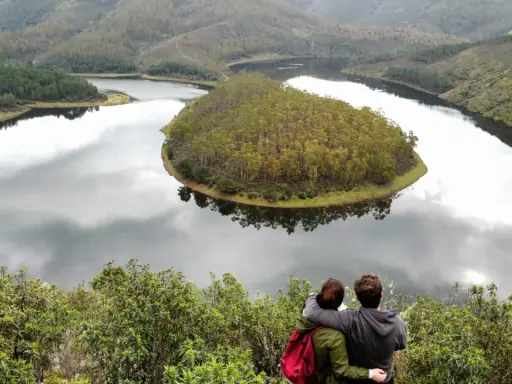 Pareja abraza contemplando el meandro del río en Las Hurdes, un paisaje de colinas verdes y agua serena.