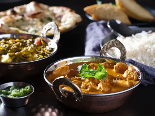 Delicioso pollo tikka masala cremoso, acompañado de arroz basmati, pan naan y una guarnición verde.
