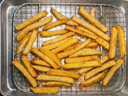 En hög med gyllene, krispiga pommes frites ligger på ett galler i en plåt. Perfekt för en snabb fika!