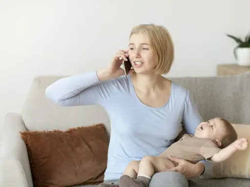 Zestresowana mama rozmawia przez telefon, trzymając dziecko, które wymiotuje po mleku modyfikowanym.