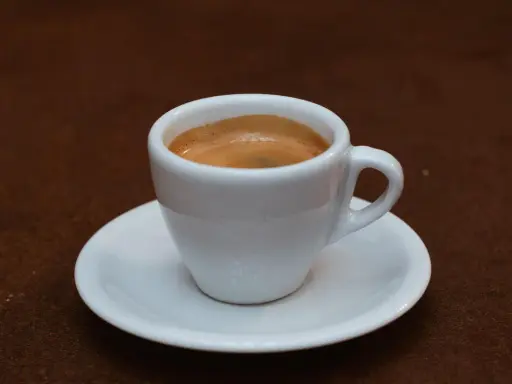 Ein kleiner weißer Becher mit cremigem, doppeltem Espresso, italienisch zubereitet, steht auf einer Untertasse.