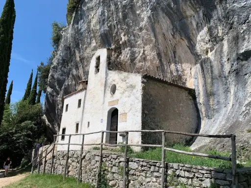 Piccolo eremo di San Valentino incastonato nella roccia, con un campanile a vela e un sentiero che conduce al suo ingresso.