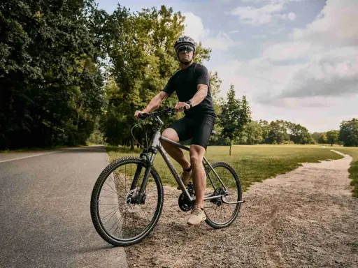 Mężczyzna w kasku i okularach jedzie na rowerze typu cross po ścieżce w parku.