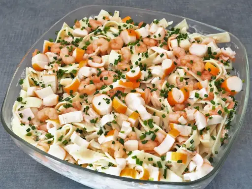 Salade Marco Polo : pâtes, crevettes, bâtonnets de surimi et ciboulette dans un plat en verre.