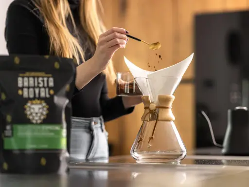Frau bereitet Kaffee zu, um zu zeigen, was ist Caffe Latte. Kaffeepulver rieselt aus Löffel in Filter.