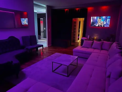 Nowoczesny salon z fioletowym oświetleniem. Na ekranie telewizora widać scenę, która może sugerować, czym jest swingowanie.