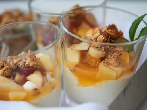 Leckeres Joghurt Dessert mit Früchten und Granola in Gläsern, garniert mit Minze.