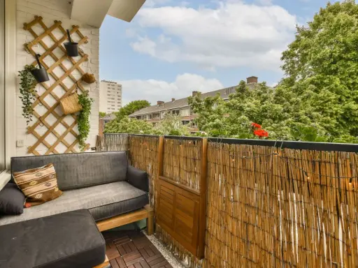 Balkon osłonięty matą bambusową, z wygodną sofą i ozdobną kratką na ścianie. Idealne miejsce, by osłonić balkon i cieszyć się prywatnością.