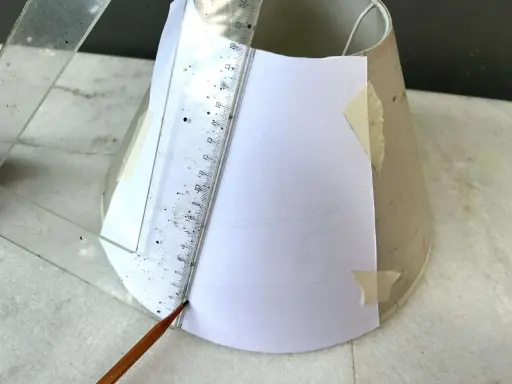 Un crayon et une règle marquent un gabarit en papier sur un abat-jour DIY.