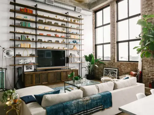 Soggiorno con scaffalatura a tutta parete, TV e divano bianco. Il soffitto alto 5 metri crea un'atmosfera ariosa, accentuata dalle grandi finestre.